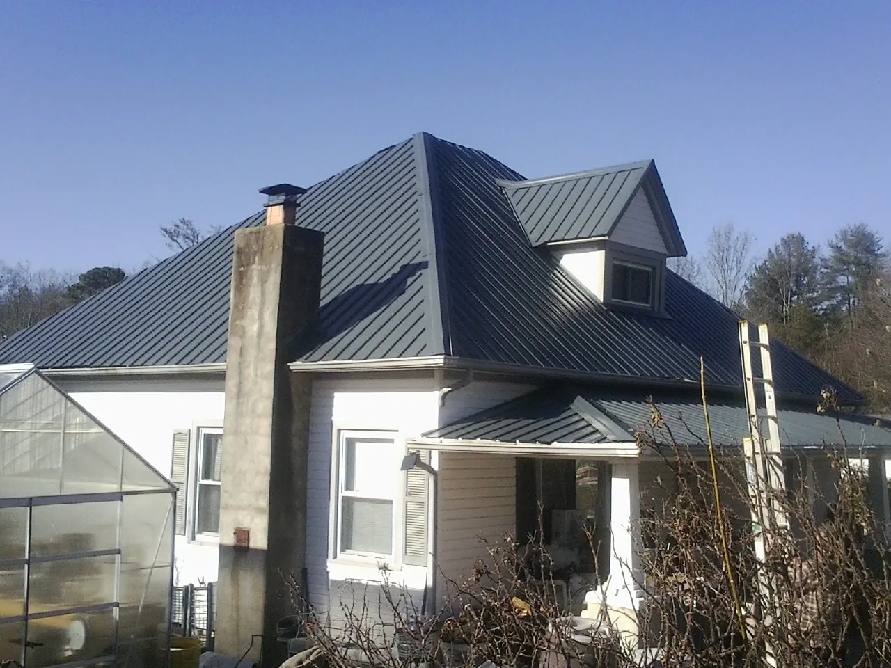 Dark blue standing seam metal roof on a white farmhouse with dormer — Slate & Tile Roof Repair by Roofing Brothers in Winter Garden