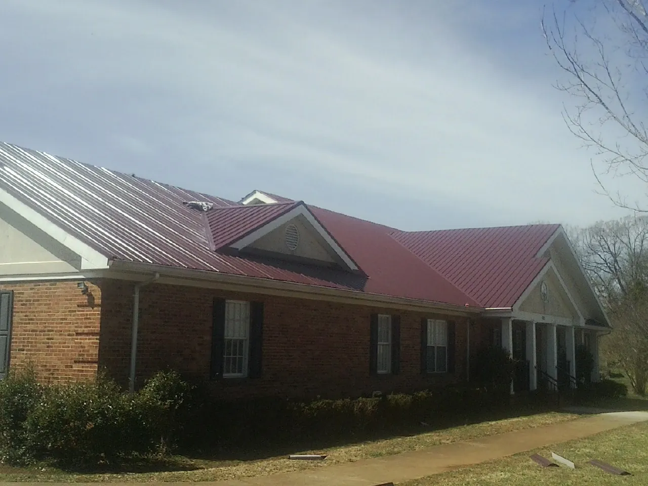 Red metal roof with gabled entries on a long brick building, from a Hail Damage Roof Repair job in Winter Garden