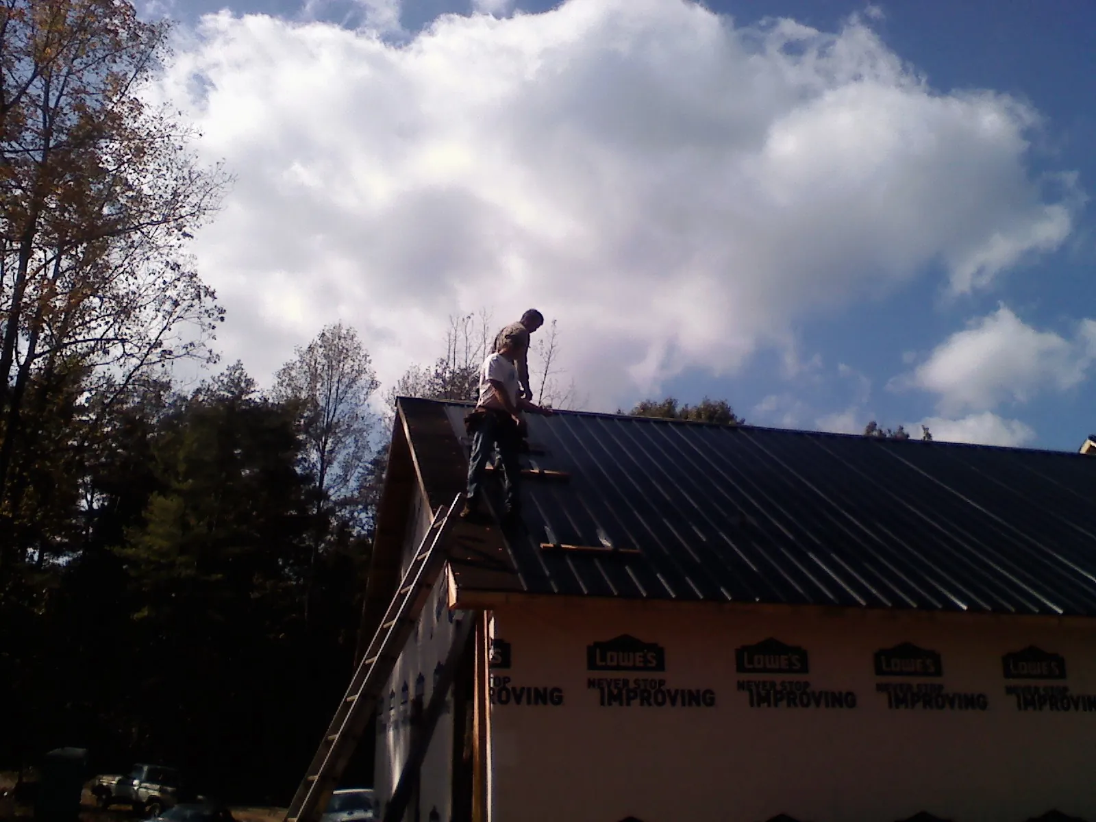 Roofer fastening dark metal panels high against a cloudy sky, from a Roof Inspection job in Winter Garden